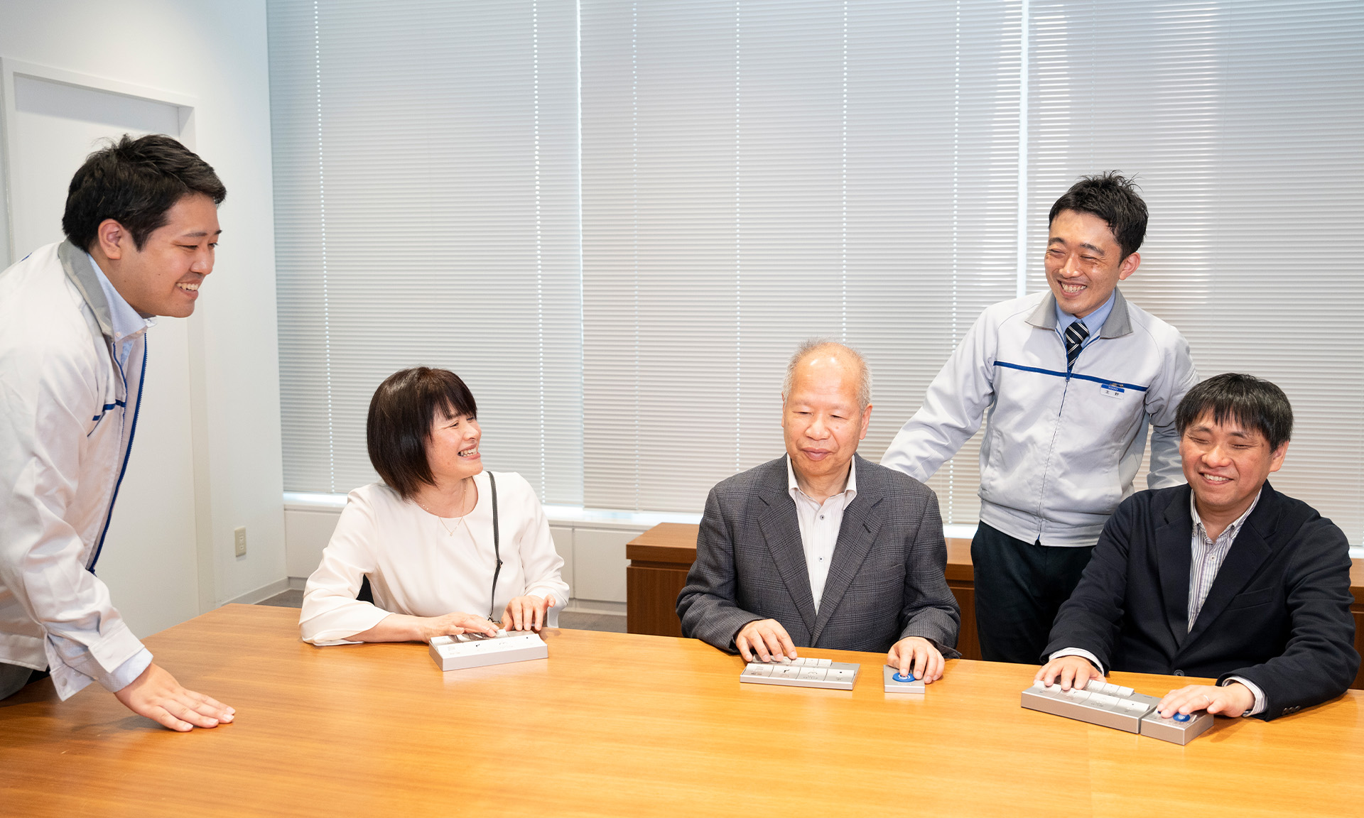 椅子に座り、リモコンを触りながら談笑する西島さん、長岡さん、大河内さん。内藤さんと北野さんが横や後ろに立ってその様子を笑顔で見ている